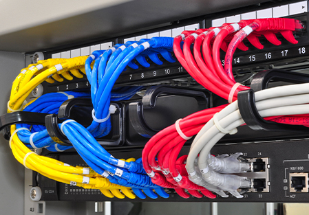 A close-up of a network server rack showing neatly organized yellow, blue, red, and white Ethernet cables connected to patch panels and network ports.